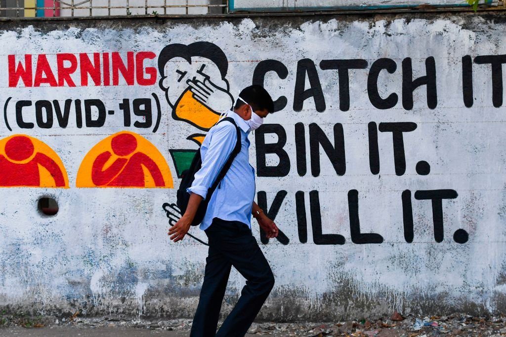 A pedestrian wearing a facemask amidst fears over the spread of the Covid-19 coronavirus walks past a wall graffiti creating awareness about the pandemic, in Mumbai on March 23, 2020.